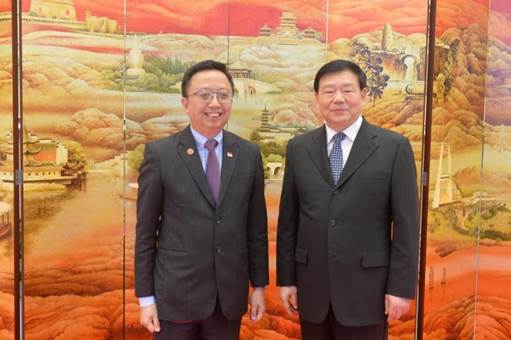 Two men in suits stand before a painted folding screen of Chinese landscape.